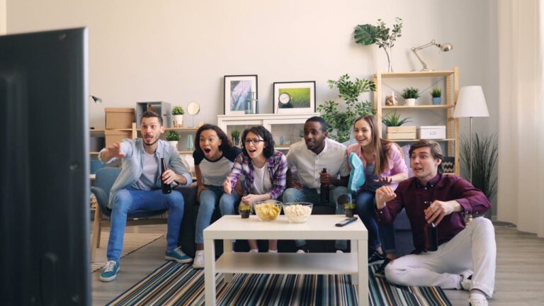 A lively group of diverse friends cheering while watching a sports game together in a cozy living room.