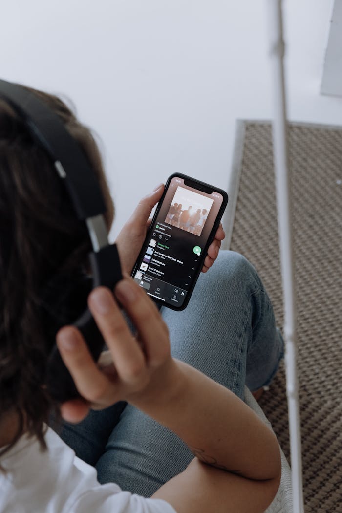 A young woman wearing headphones, relaxing at home, listens to music on her smartphone.